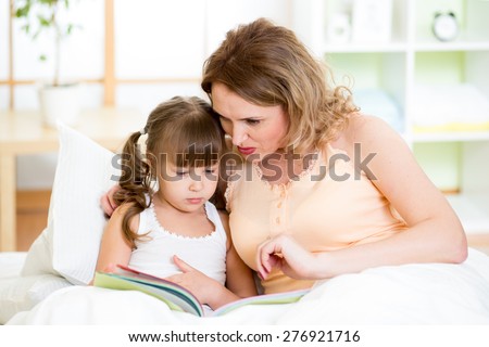 Happy mother and kid daughter read a book together in bed