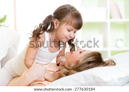 Cute mom and child daughter embracing and kissing in bed at bedroom