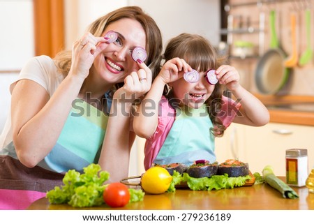 Funny mother and daughter playing with vegetables in kitchen, family and healthy food
