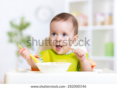 happy cute baby kid eating food itself with spoon