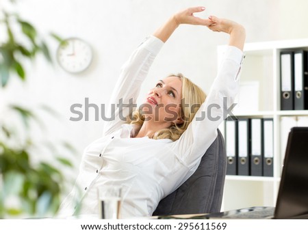 Middle-aged businesswoman with arms up relaxing in office during pause