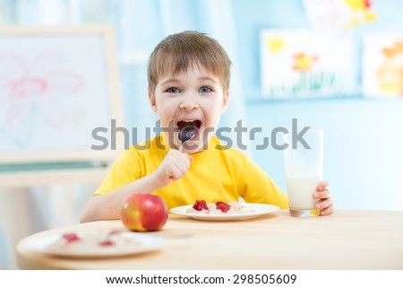 cheerful kid boy eating healthy food at home or kindergarten