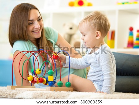 Kid boy plays with educational toy in nursery at home. Happy mother looking at her smart son.