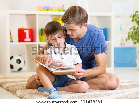 kid boy and his father read a book on floor indoors