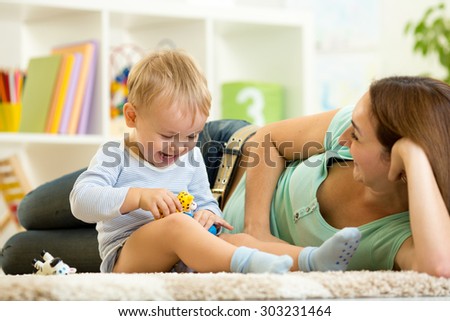 happy child boy holds animal toy playing with mom in nursery
