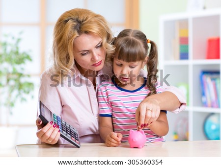 family - middle aged mother and kid daughter with pink piggy bank and calculator