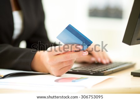 Businesswoman holding credit card in hand and entering security code using laptop keyboard