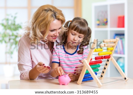 Mother and daughter putting coins into piggy bank. Child counting and saving money.