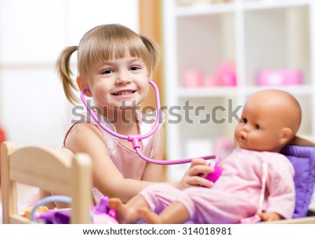 child girl playing doctor role game examinating her doll using stethoscope sitting in playroom at home, school or kindergarten