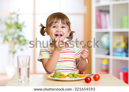 happy kid girl eating healthy food vegetables at home in nursery