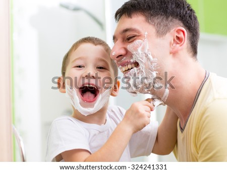Cheerful father and his kid son playing in bathroom. Child putting shaving cream on daddy face.