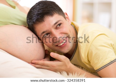 Happy husband listening to belly of  his pregnant wife