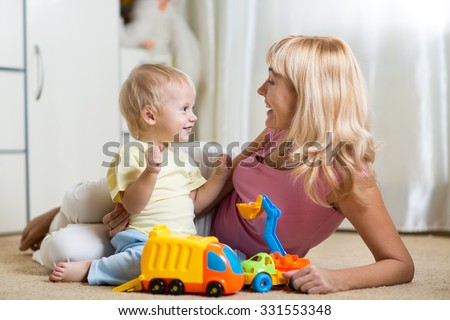 Smiling mother and child boy play with car toys together at home