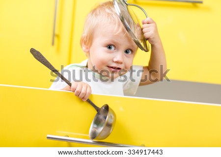 Funny kid boy sitting inside yellow opened kitchen box with laddle