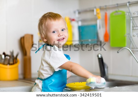 Adorable toddler child washing dishes in kitchen. Little boy having fun with helping to his mother with housework.