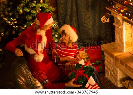 Happy family - mom, dad and daughter in Santa hats with gifts sitting at Christmas tree near fireplace