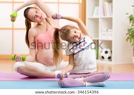 Pregnant woman and her elder child daughter doing fitness exercises  with dumbbells