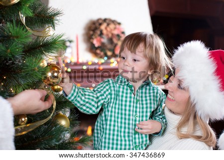 Child boy helps his parents to decorate family Christmas tree