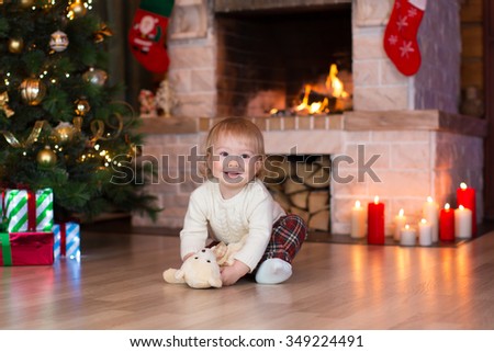 Kid boy playing with toy gift on Christmas eve at fireplace. Decorated living room with traditional fire place.