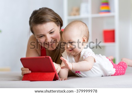 Family - mother and baby with tablet on floor at home. Woman and child girl relaxing at tablet computer.