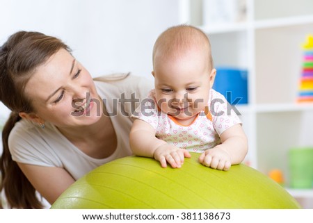 Mother with child doing exercises with green gymnastic ball at home. Concept of caring for the baby\'s health.