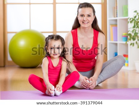 Young mother with little daughter exercising in gym at home
