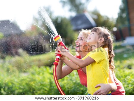 Little gardener girl with mother watering on lawn near house