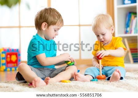 Children boys play with educational toys in preschool or kindergarten. Toddler kid and baby build pyramid toys at home or daycare.