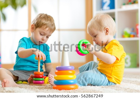 Children playing together. Toddler kid and baby play with blocks. Educational toys for preschool and kindergarten child. Little boys build pyramid toys at home or daycare.