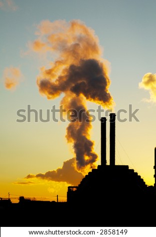 Silhouette of smoke stacks smoking up to the sky at sunset