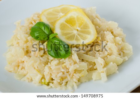 Close up on a dish of lemon risotto with a lemon slice and two leaves of basil