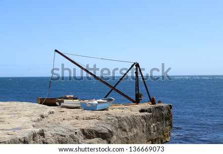 Three Boats and an Old Crane Sitting On The Side Of The Sea