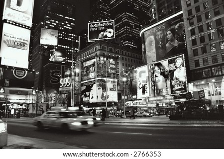 A speeding cab in the center of this black and white scene of New York\'s Time Square at night.