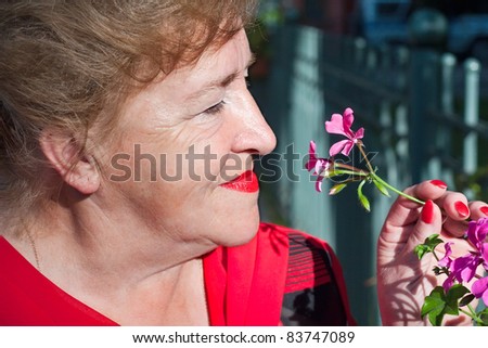 A beautiful senior lady holding a pink flower, smiling and ready to smell it.