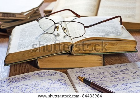 Opened notebook, pen, books and glasses on the wooden table