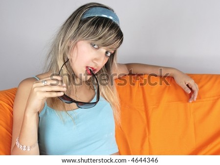 Blond Pin-up style fascinating girl with light blue shirt set on orange sofa, taking sunglasses in her hand.