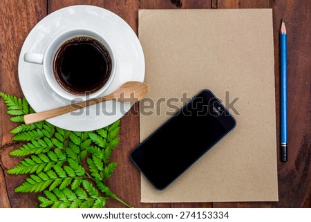 Cup of coffee, brown paper, pencil with smart phone on wooden table, top view