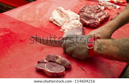 Butcher wearing safety gloves cutting meat on the top of cutting board