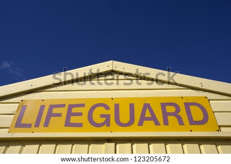 Yellow lifeguard sign, on yellow lifeguard hut, isolated against a blue sky.