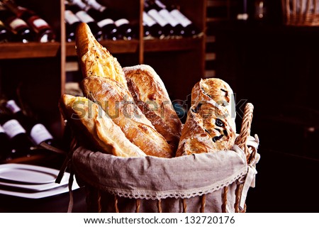 Fresh bread in basket witn bottles of wine on background