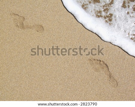 Female footprints on the beach with crestwaves coming from the side.