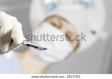 Perspective of a patient on a operating table who sees the doctor above him with a scalpel in his hand. Focus only on the scalpel.