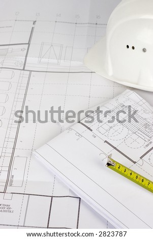 Hardhat and measuring tape lying on construction plans. Focus on the measuring tape.