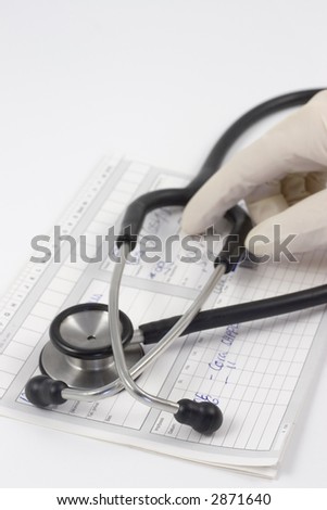 Stethoscope on a medical record. In the background a hand with medical rubber glove. Focus on the foreground on the bows of the stethoscope.