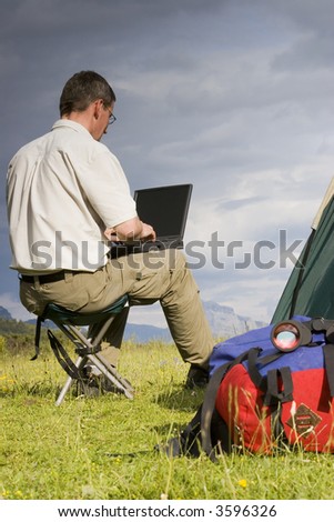 Man working with laptop beside his tent in the mountains