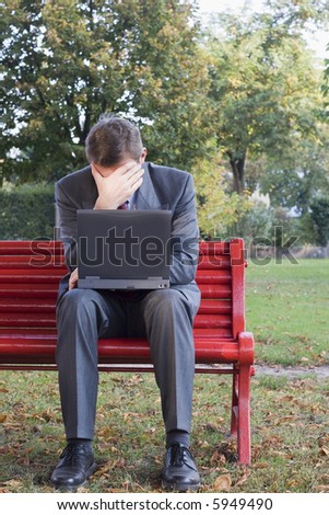 Tired businessman with laptop sitting on a park bench