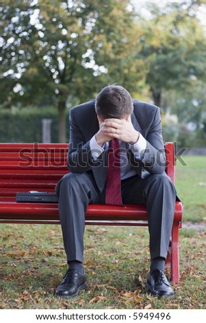 Worried businessman sitting on a red park bench