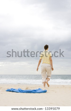 Woman walking on a beach. Focus on the towel in the foreground