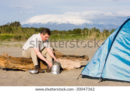 Man cooking beside his tent in front of a mountain with snow