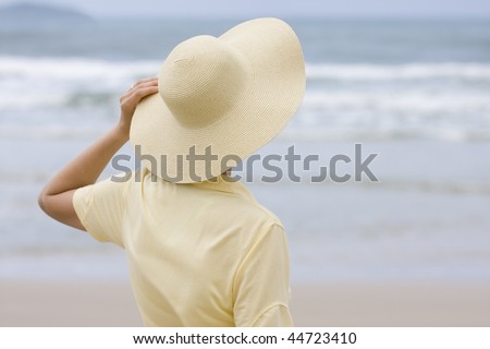 Woman with yellow hat and shirt looking at the sea - focus on the hat
